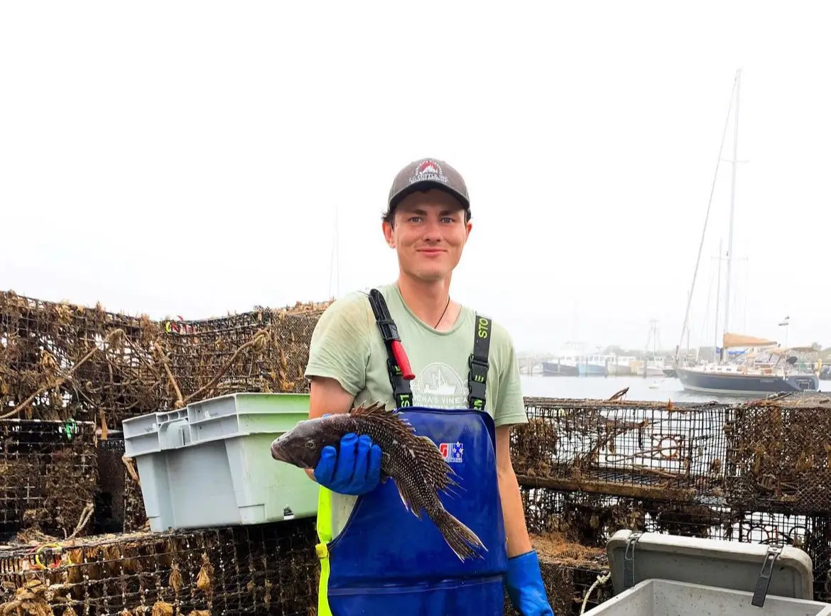 Young fisherman holding up fish while standing on fishing boat in Menemsha